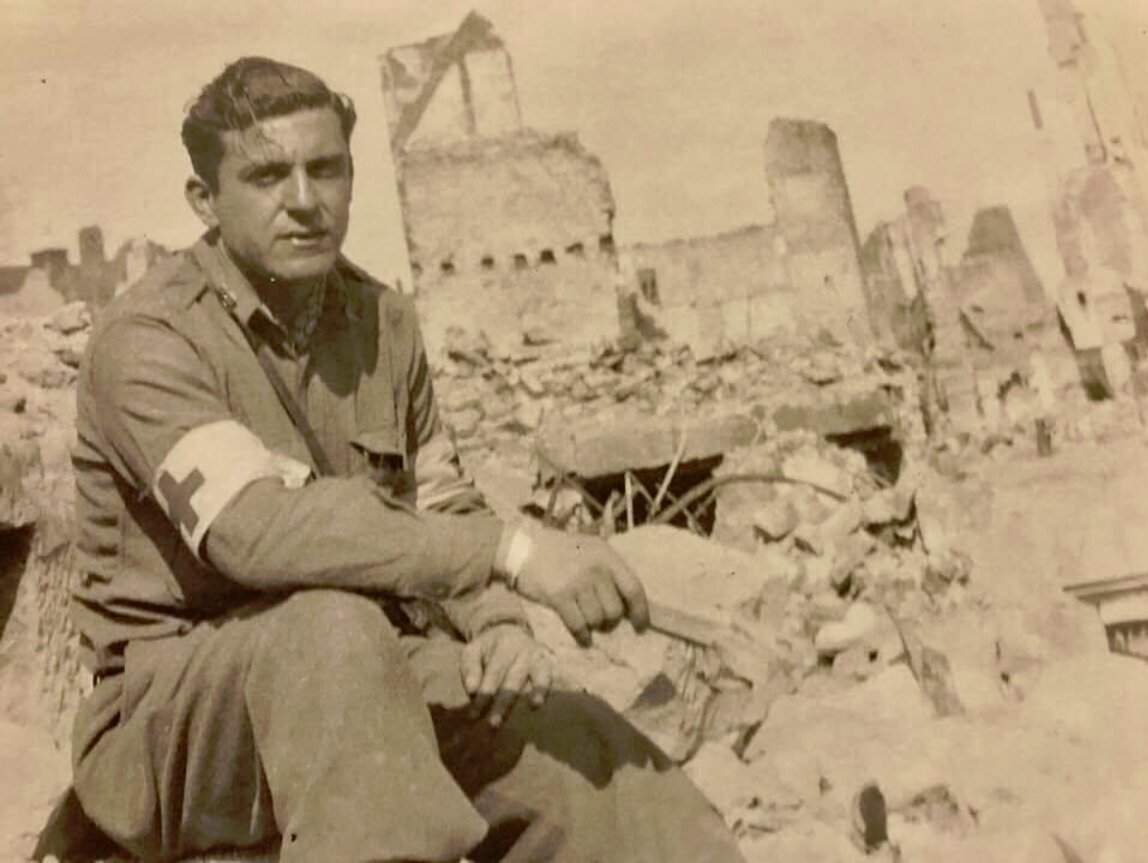 John Lazare, Red Cross armband, seated on rubble — European Theater, 1945